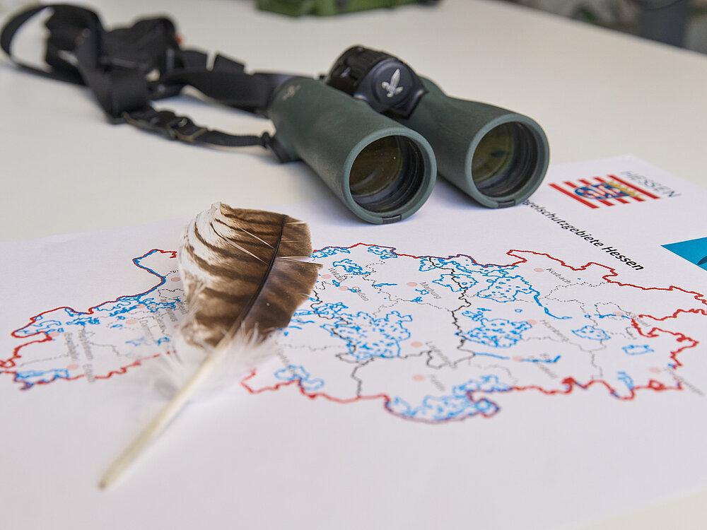 Ein Fernglas, eine Feder und eine Karte liegen auf einem Tisch.