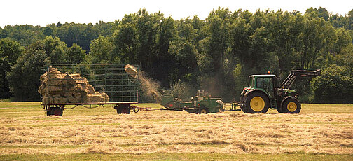 Traktor mit Ballenpresse und Ladewagen beim Aufladen von Heuballen